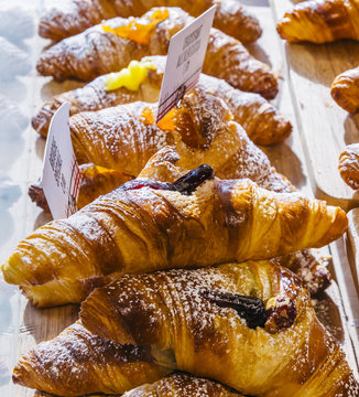 Various flavours of croissant or as in Italy their called brioche on display in a bakery in Milan, Italy with a price and sign - Albicocca means jam in Italian