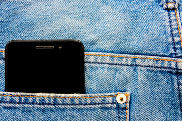 Black smart mobile phone in back blue jeans pocket denim background texture.