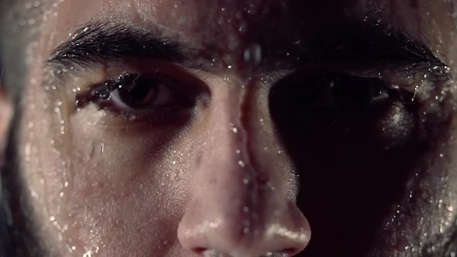 close up shot of the face of a dark-bearded man who stands in the rain in the studio