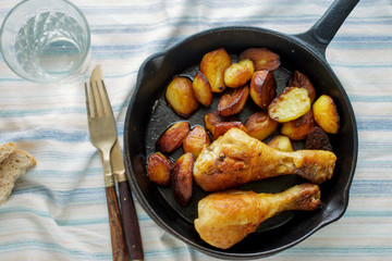 Fried chicken legs, fried potatoes in frying pan, top view