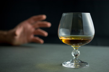 hand reaches for a glass of whiskey or cognac or alcohol drink, alcoholism and alcohol abuse concept, defocused, selective focus, close up, gray table, can be used as a background