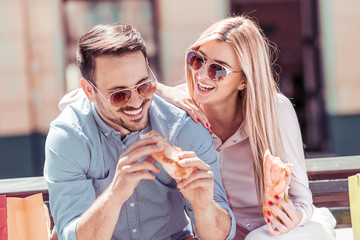 Couple eating sandwich and talking outdoor in city after shopping.