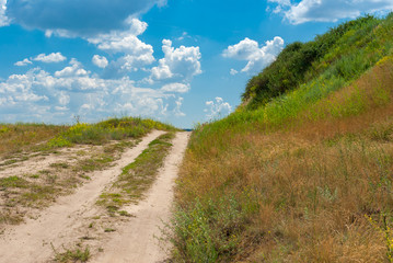 Fototapeta na wymiar Sandy country road leading on a hill at summer season in Ukraine