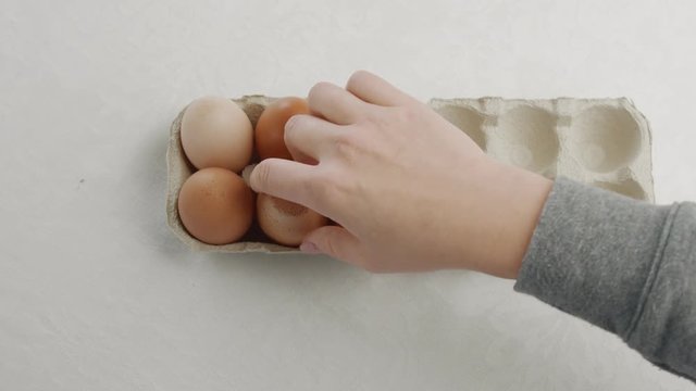 woman's hand open an eggbox with brown eggs ant take off oneof them