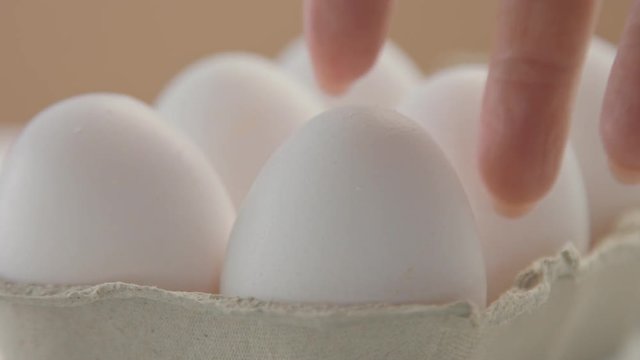closeup of egg box with white eggs and woman's hand take out one of it. white egg texture closeup