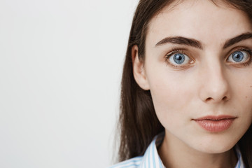 Close-up side portrait of gentle pretty european student looking at camera while standing against gray background. Woman with magnificent blue eyes waits till her boyfriend take photo of her