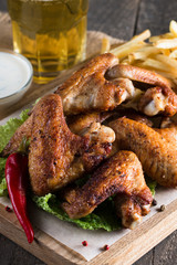 Close-up photo of bbq chicken wings with fries and beer. Barbeques meat with sauces, ketchup, mayonnaise. Fast and junk food concept. 