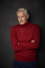 Fototapeta na wymiar Casual senior man portrait. Handsome elderly man wearing red turtle neck sweater and looking at camera while standing against at dark background.