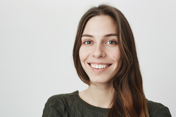 Obraz premium Close up portrait of young beautiful attractive girl, smiling cheerfully looking at camera over white background. Woman enjoys conversation with her mates, expresses positive emotions.