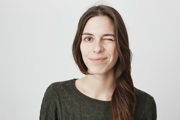 Obraz premium Close up picture of young pretty european girl in casual dark green sweater winking and smiling over white background. Mimic and expression concept. Woman says to her lover that everything is fine