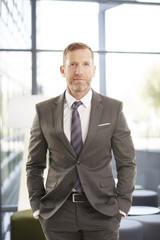 Successful businessman portrait. Middle aged financial director businessman sitting at office and looking at camera. Wearing elegant suit with tie.