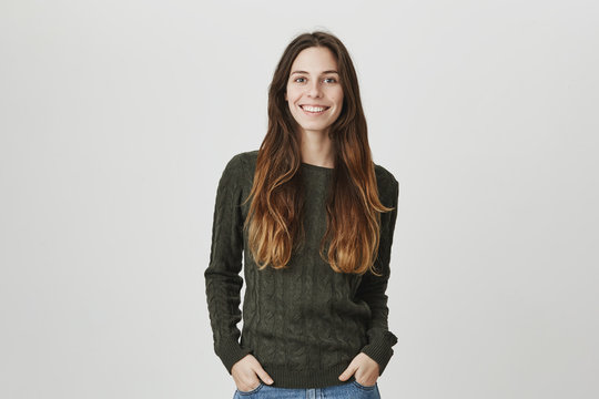 Portrait of beautiful european student with long brown hair wearing casual warm sweater with wide broad smile and hands in pockets over white background. Girlfriend is waiting for her boyfriend