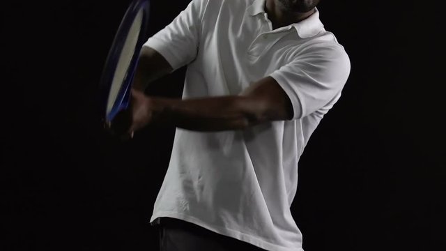 Muscle tennis player in white polo hitting the ball on black background, slow