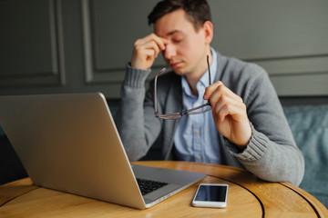 Feeling sick and tired. Frustrated young man massaging his nose and keeping eyes closed while sitting while working in cafe.