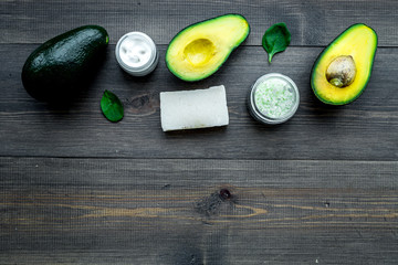 Cosmetics based on avocado oil. Cream, soap, spa salt on dark wooden background top view copy space