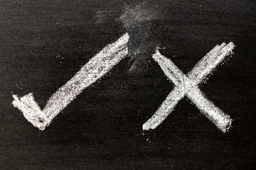White color chalk hand drawing as check mark of right and wrong shape on black board background