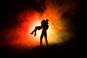 Naklejka na ściany i meble Love Valentine`s Day concept.Sillhouette of sweet young couple in love standing in the field and hugging on dark toned foggy background. Decoration with doll figures on table shot.