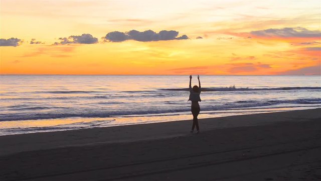 Pretty young woman walking happily along the beach at sunset. A video taken from a distance with a static image and the woman moves slowly from the camera and shows pleasure and happiness in the beaut