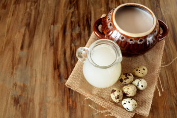 Obraz premium Milk whey, quail eggs and a clay pot on a wooden background. Farm products