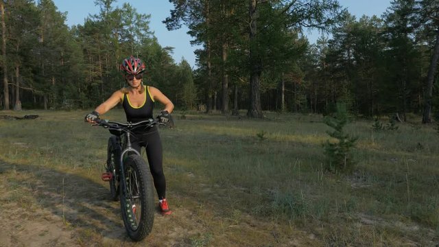 Fat bike also called fatbike or fat-tire bike in summer riding in the forest. Beautiful girl and her bicycle in the forest. She puts her bike more comfortable to roll down beautifully.