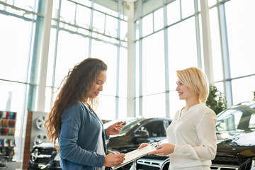 Profile view of mixed race curly customer holding car key in hand and signing contract while...