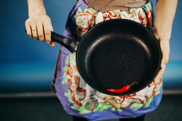 The girl with a frying pan. Are red sharp Chile pepper on a frying pan