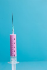Close-up of medical syringe with pink medicine on blue background. Health care, medicine and pharmacy concept