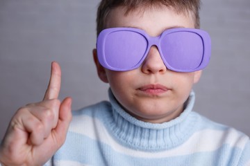 Cute boy in violet sunglasses with opaque lenses pointing upwards