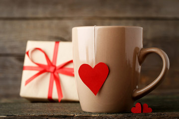 Cup of tea with red heart and gift box on wooden table