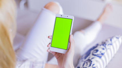 Woman at home relaxing reading on the smartphone with pre-keyed green screen 