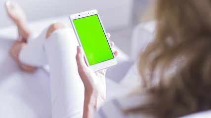 Woman at home relaxing reading on the smartphone with pre-keyed green screen 