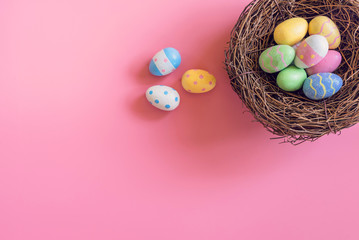 Colorful easter eggs in nest on pink pastel color background with space.