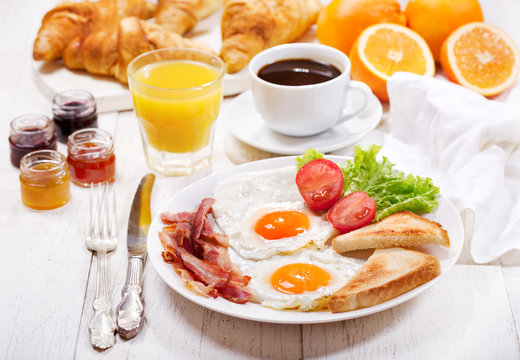 breakfast with fried eggs, croissants, juice, coffee and fruits