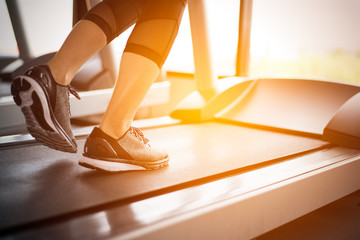 Lower body at legs part of Fitness girl running on running machine or treadmill in fitness gym with sun ray. Warm tone. Healthy and Exercise activity concept. Workout and  Strength training theme.