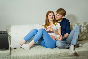 beautiful young couple guy with a girl with red hair sitting on the couch and drinking tea