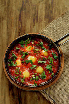 Fried eggs with tomato sauce and parsley in a cast iron pan on wooden background. Shakshuka a traditional meal of the Jewish cuisine