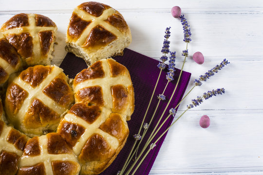 Easter hot cross buns witt lavender flower, and chocolate eggs on violet napkin and wooden white table.