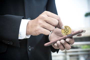 man wearing business suit holding Gold Bitcoin from mobile phone, transfer money concept