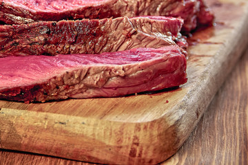 Fried meat with blood. Sliced pieces of a well-made juicy steak close-up. Wooden background. Rustic stile. Selective focus.