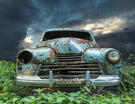 An old vintage rustic baby blue colored car on a field with cloudy sky background