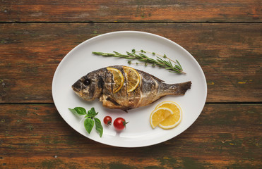 Whole grilled dorado with lemon slices on table