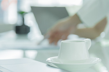 A coffee cup with white plate on the office desk.