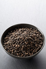Raw, natural, unprocessed black pepper peppercorns in black bowl