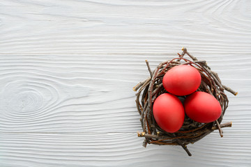 Easter background with red eggs in the nest on wooden table. Top view with copy space