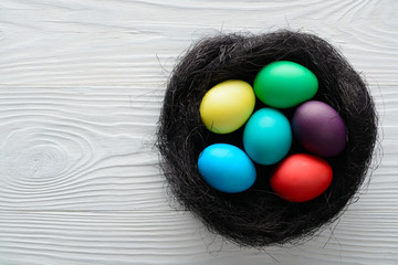 Multicolored Easter eggs in a nest on the wooden table. Top view with copy space