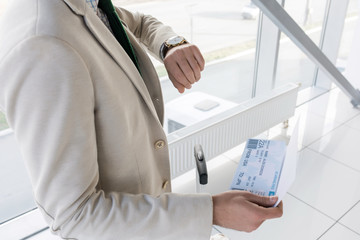 High angle view of unrecognizable businessman checking time and holding airplane tickets while...
