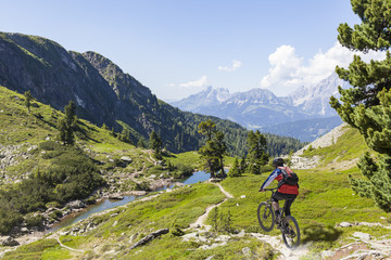 Fototapeta na wymiar Mountainbiker downhill on Reiteralm with mountain Dachstein in Styria Austria