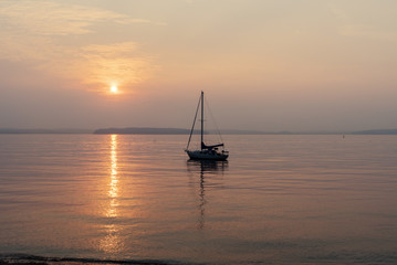 Silhouetted sailboat anchored off shore at sunset