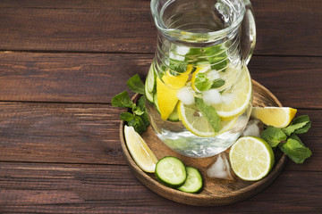 Detox drink with cucumber, lemon and mint in glass jug on a wooden background. Copy space. Food background