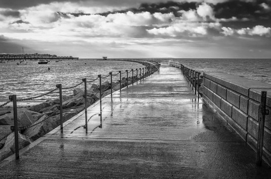 black and white image of the breakwater known as Neptune's Arm in Herne Bay, Kent, UK during a high tide when the wet walkway was closed due to waves breaking over the top of it in the wind.